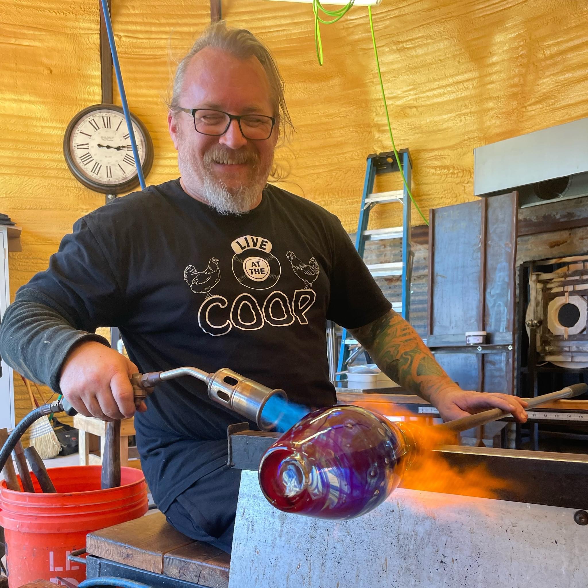 happy glass blower torching a vase with a fluffy torch.